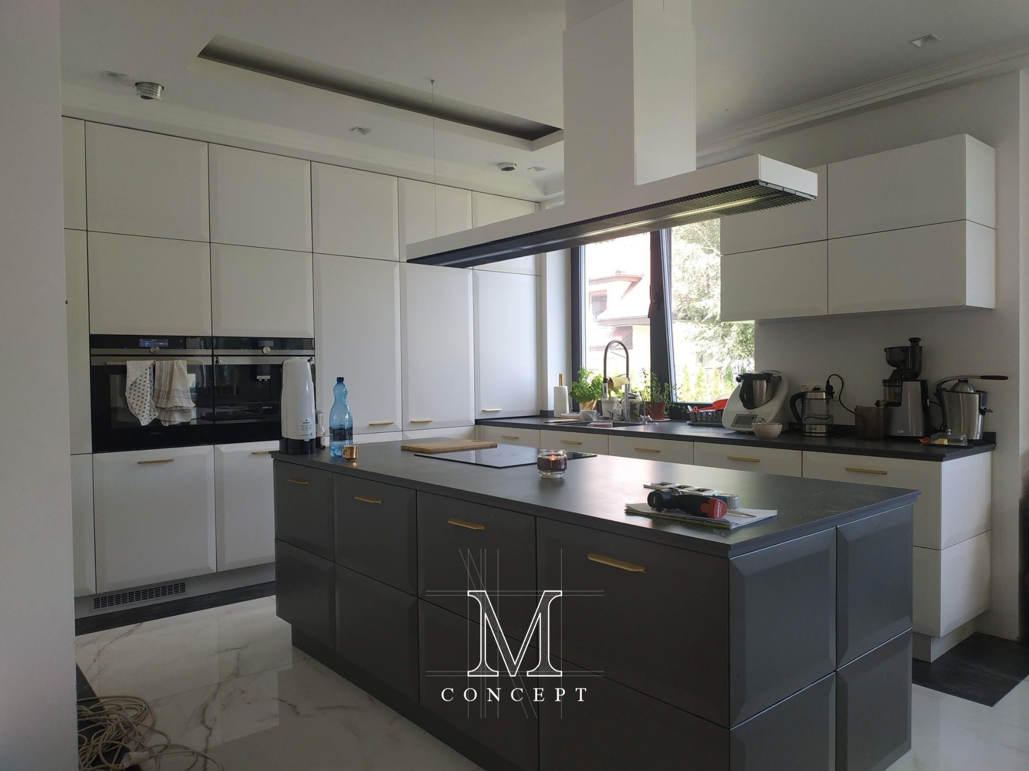 Nowoczesna kuchnia z frezowanymi frontami, blatem Atlas Plan Grey Stone i wyspą z szufladami, oświetlona przez wiszący okap. Widoczny sprzęt AGD Siemens.