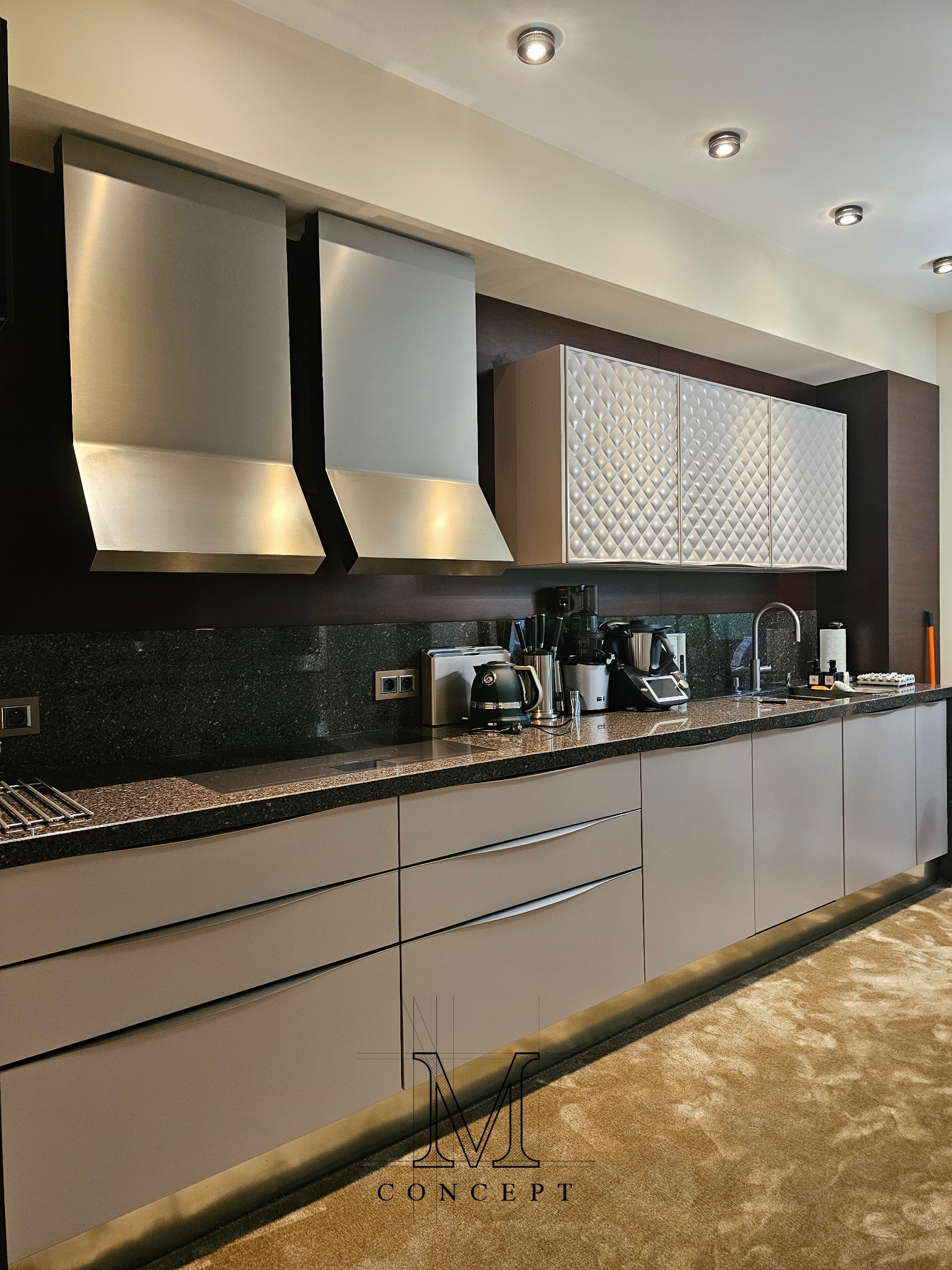 Nowoczesna kuchnia z frezowanymi frontami MDF, granitowym blatem i okładziną. Dwa srebrne okapy nad płytą. Sprzęt AGD na blacie. Uwagę przykuwają frezowane fronty.