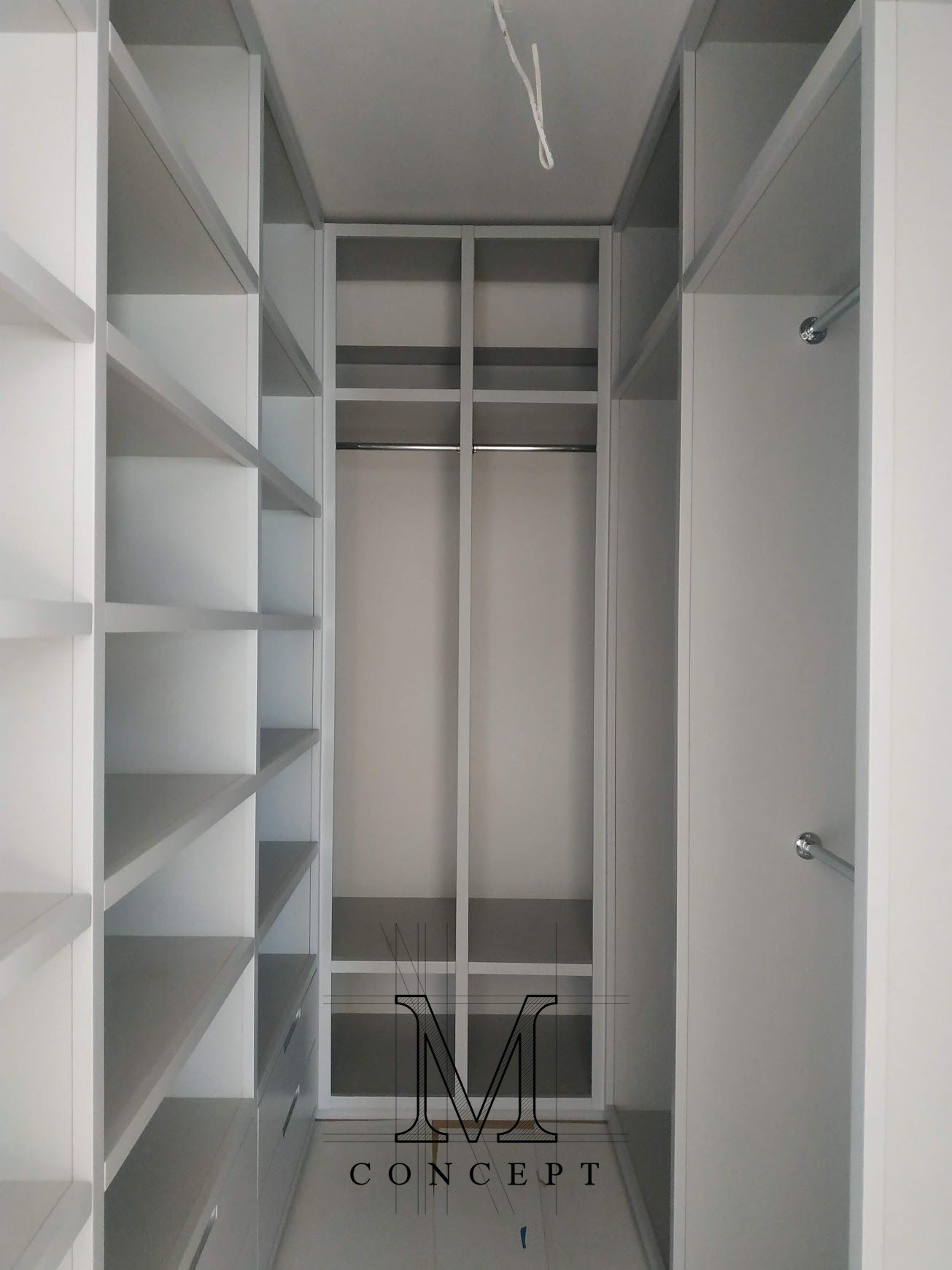 Wnętrze garderoby na wymiar z białymi półkami i drążkami na ubrania, widok z perspektywy wejścia. Minimalistyczny design, jasna kolorystyka, zorganizowana przestrzeń.