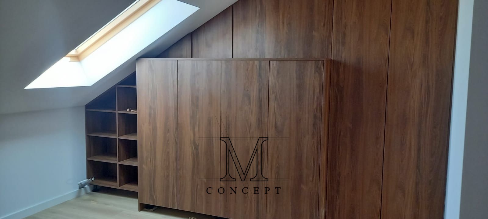 Zabudowa pod skosem z drewnianą szafą z logo firmy, półki wnękowe obok okna dachowego. Realizacja szafy na wymiar z charakterystycznym wykończeniem.