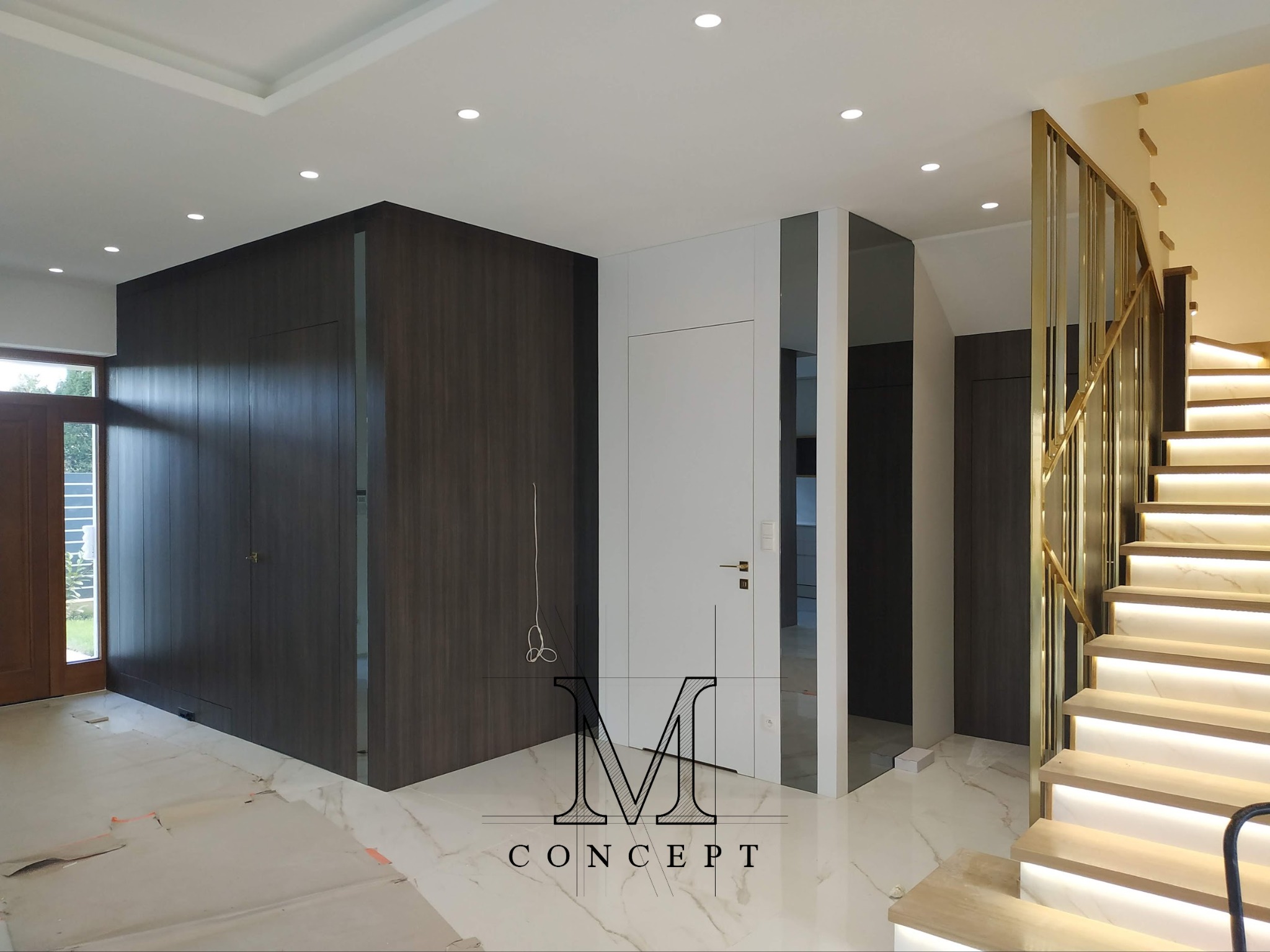 Nowoczesny hol z drewnianą szafą w zabudowie, lustrem i podświetlanymi schodami. Marmurowa podłoga w trakcie montażu. Minimalistyczny design.