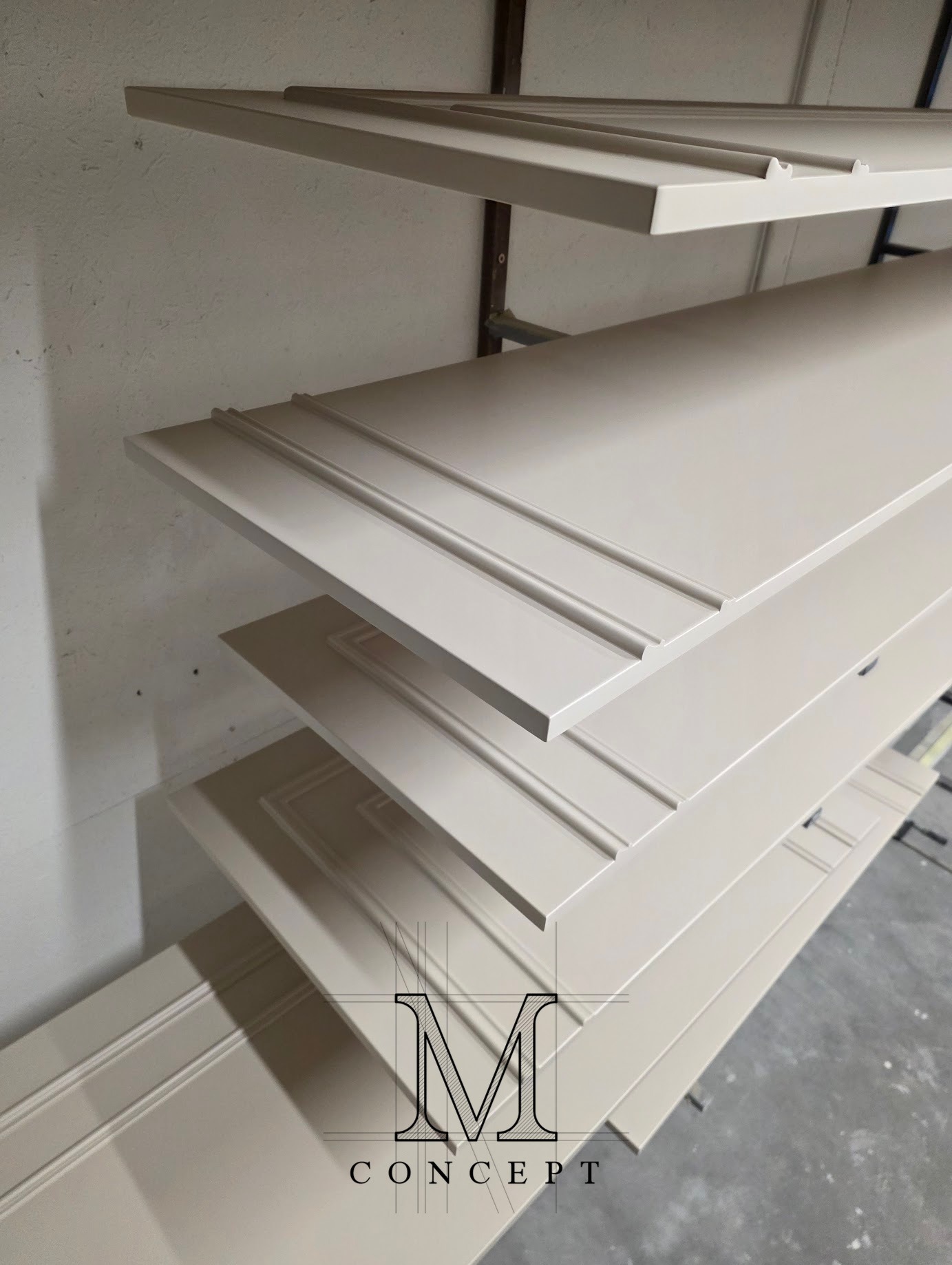 Półmatowe fronty szafy z MDF na metalowym regale, z frezowanymi detalami i logo firmy w rogu. Elementy gotowe do montażu, w jasnym odcieniu beżu.
