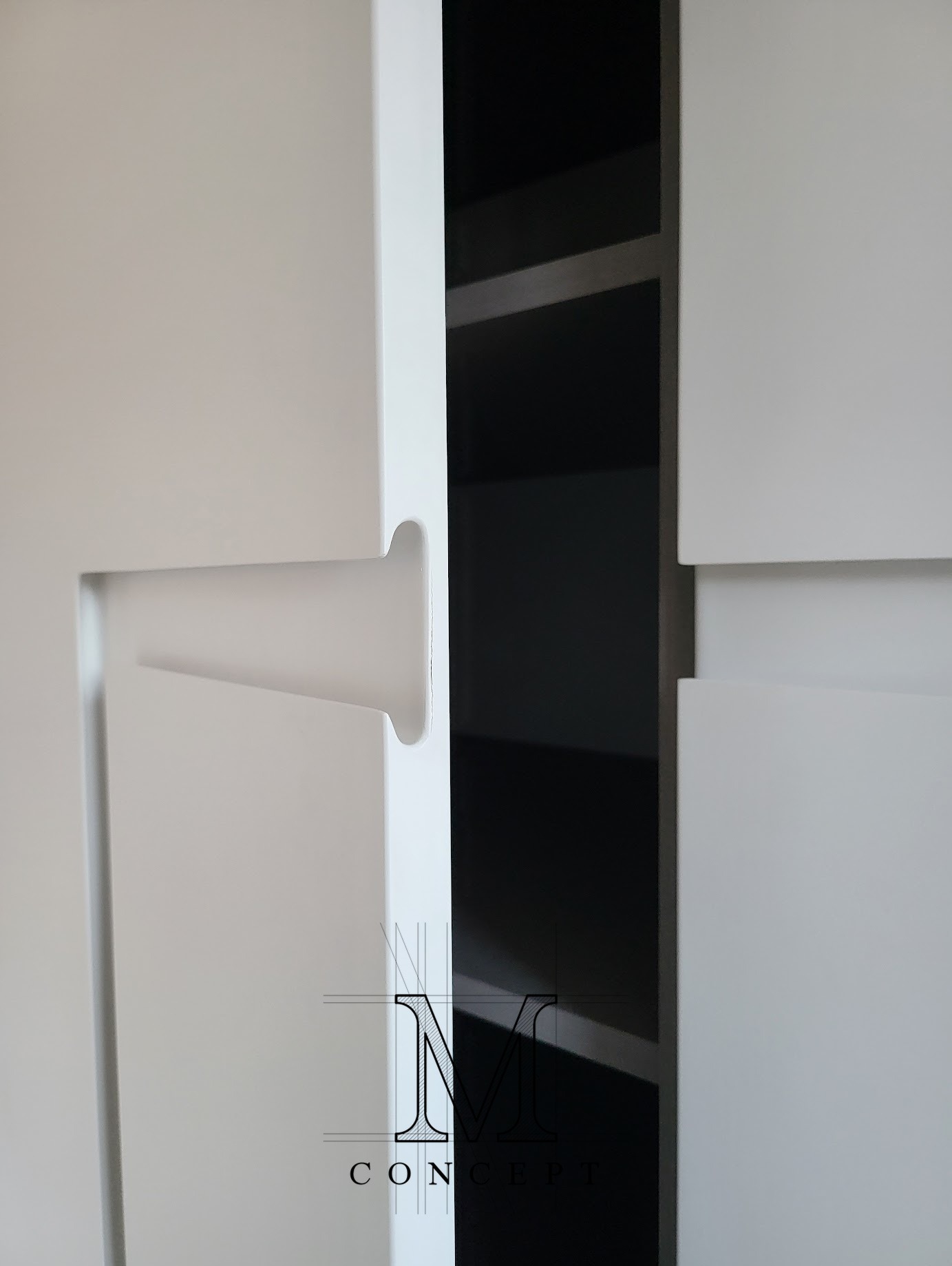 Minimalistyczna szafa z frezowanymi uchwytami w białym, półmatowym lakierze. Wnętrze szafy w kolorze grafitowym. Detal frontu z bliska.