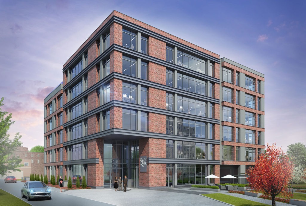 Nowoczesny budynek biurowy z ceglaną fasadą i dużymi oknami, otoczony zielenią i z zaparkowanym samochodem. Widoczni ludzie przed wejściem.