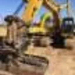 Dwa żółte, ciężkie koparki na piaszczystym placu budowy, z widocznym fragmentem niebieskiego nieba w tle.