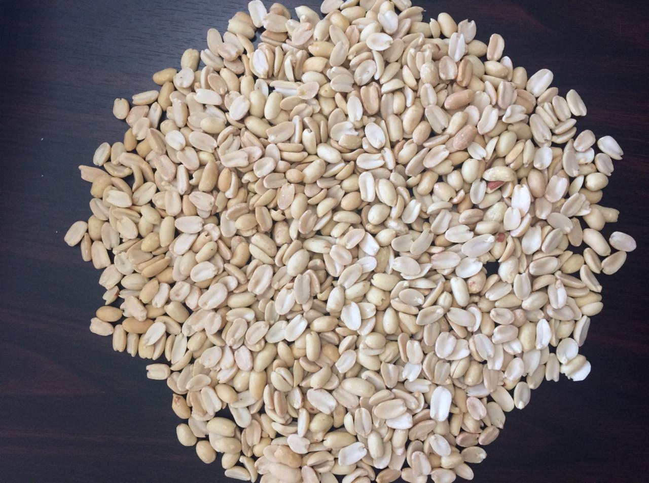 Stos łuskanych orzechów ziemnych na ciemnym, drewnianym tle, z widoczną teksturą drewna.