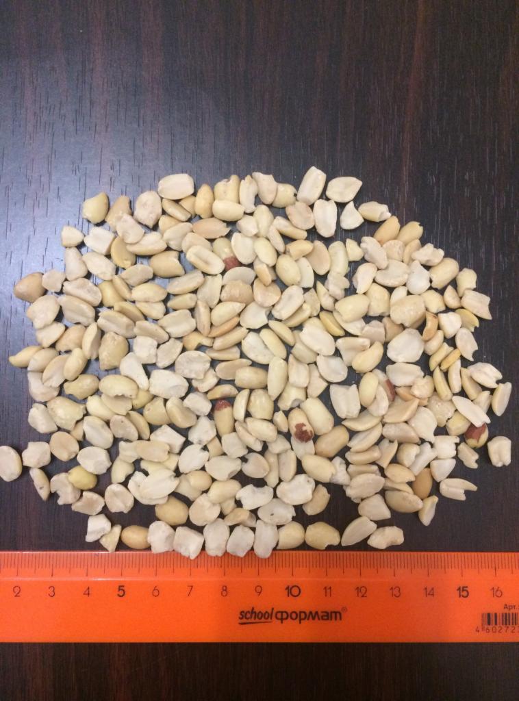 Łuskane orzeszki ziemne, nieblanszowane, rozsypane na ciemnym blacie, obok pomarańczowa linijka z podziałką centymetrową.