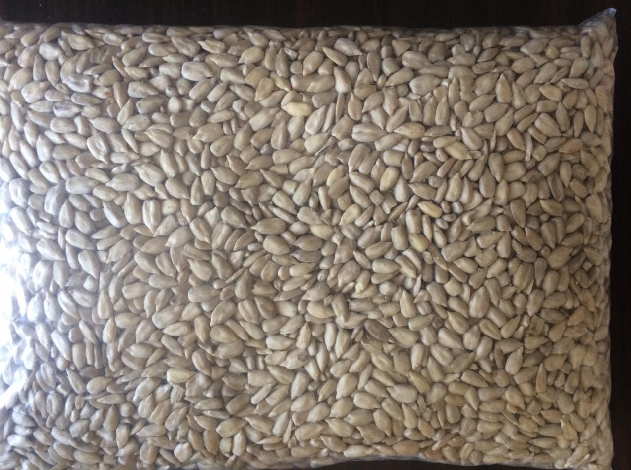 Worek wypełniony łuskanymi nasionami słonecznika o jasnej barwie, widoczne delikatne refleksy światła na przezroczystym opakowaniu.