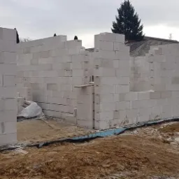 Wznoszenie ścian zewnętrznych z bloczków gazobetonowych Ytong, widoczne fragmenty rusztowania i materiały budowlane na placu budowy.