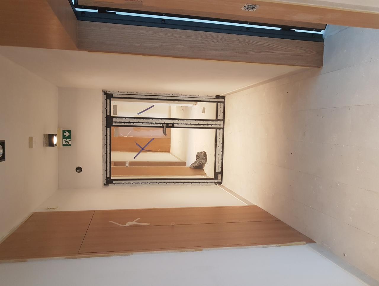 Wnętrze w trakcie remontu, widoczne ściany przygotowane do malowania, zabudowa z płyty karton gips na suficie i podłodze, okno z widokiem na schody.