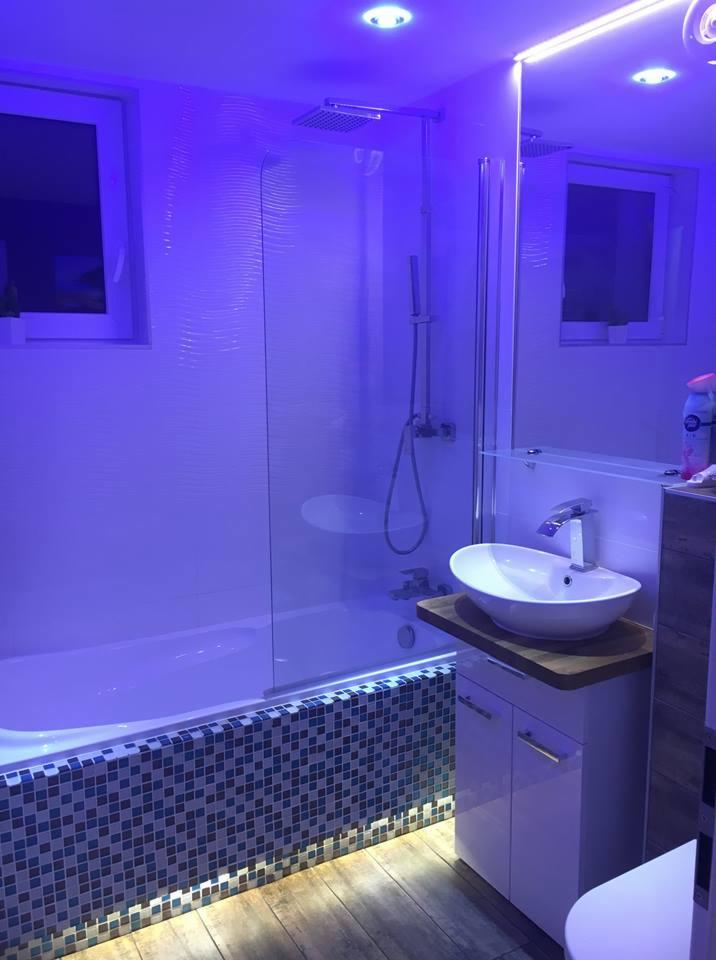 Nowoczesna łazienka z wanną za szklanym parawanem, umywalką nablatową na szafce i podświetleniem LED w kolorze niebieskim.