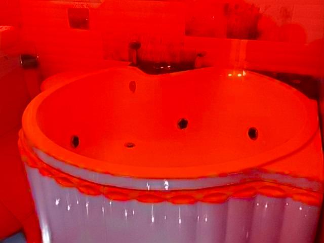 Zdjęcie przedstawia wannę z hydromasażem w łazience, z widocznymi dyszami i ozdobnym wykończeniem. Kolorystyka zdjęcia jest mocno przekłamana w kierunku czerwieni.