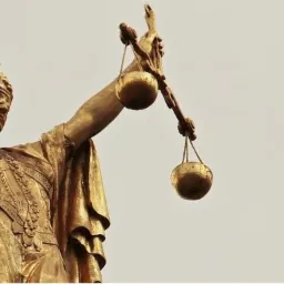 Złota statua Temidy z mieczem i wagą na tle jasnego nieba, symbol sprawiedliwości.