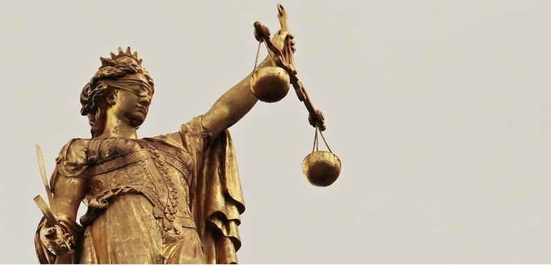 Złota statua Temidy z mieczem i wagą na tle jasnego nieba, symbol sprawiedliwości.