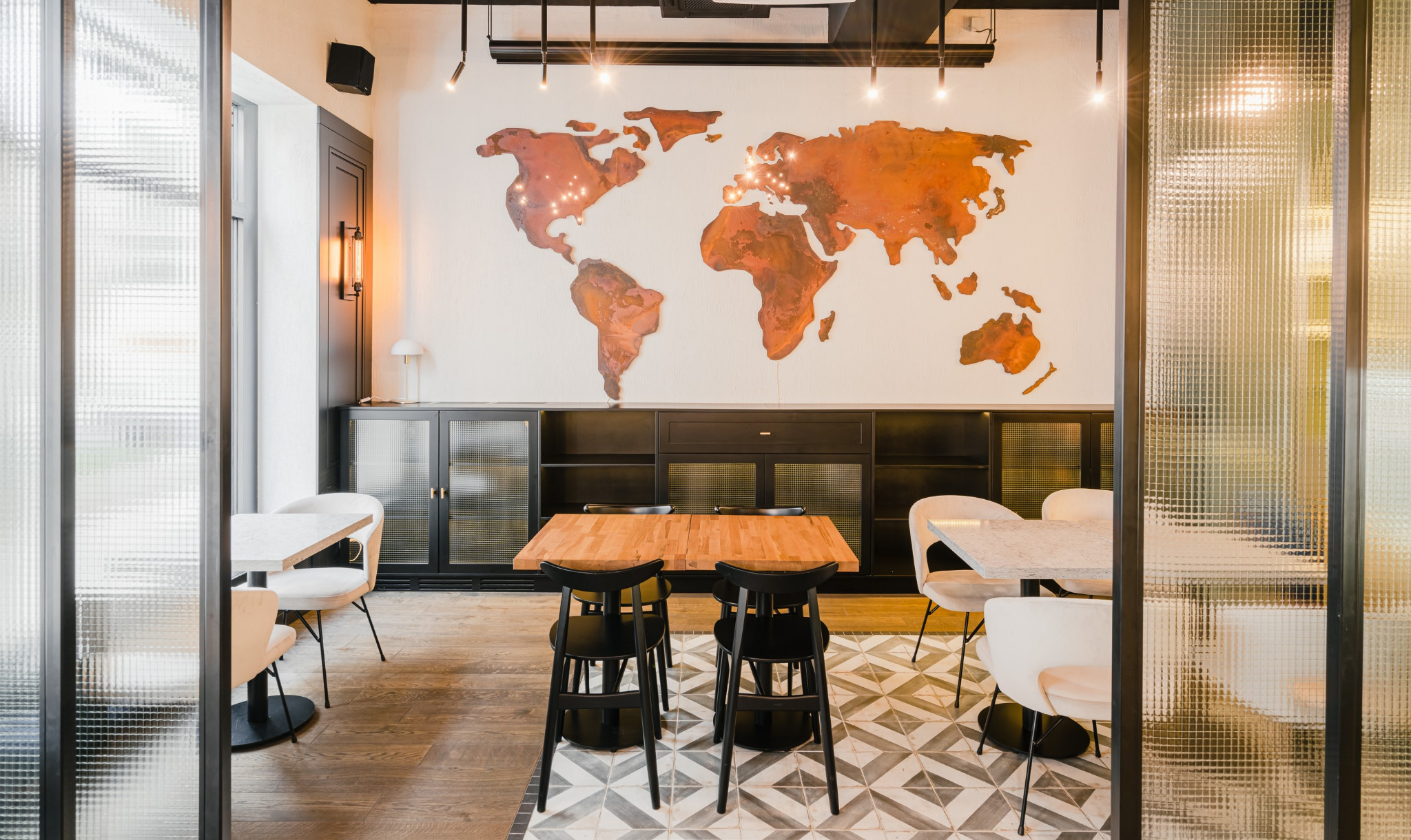Restauracja z drewnianym blatem stołu, czarnymi krzesłami i dekoracyjną mapą świata na ścianie, widok przez szklaną ścianę z fakturą.