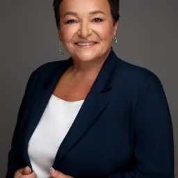 Portret uśmiechniętej kobiety w granatowej marynarce i białej bluzce, z krótkimi ciemnymi włosami i złotymi kolczykami na szarym tle.