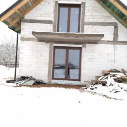 P.H.U. Para- door Łukasz Zadański - Surowy stan budynku w zimowej scenerii z zamontowanymi oknami z brązowymi ramami, widoczne drewniane elementy konstrukcji dachu i białe bloczki.