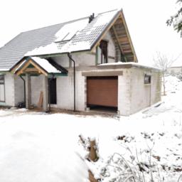 P.H.U. Para- door Łukasz Zadański - Niedokończony dom jednorodzinny w zimowej scenerii, widoczna drewniana brama garażowa w trakcie montażu, okna z brązowymi ramami, oraz ośnieżony dach pokryty szarą dachówką.