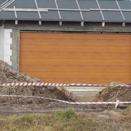 P.H.U. Para- door Łukasz Zadański - Nowa, drewnopodobna brama garażowa segmentowa w surowym stanie, widoczna ziemia i taśma ostrzegawcza.