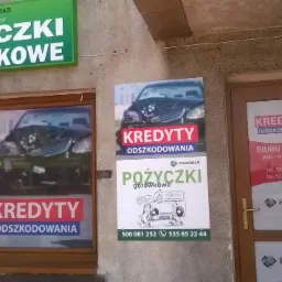 Fasada budynku z szyldami i plakatami informującymi o ofercie pożyczek gotówkowych i kredytów odszkodowawczych firmy Parkmar Łukasz. Na plakatach widoczny rozbity samochód.