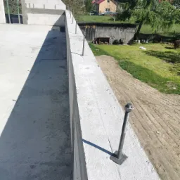 Wzniesiona ściana z betonu komórkowego z wystającymi metalowymi prętami kotwiącymi, widok z góry na plac budowy i otoczenie.