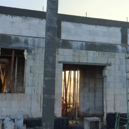 Dawid Wilk TYNK-TECH - Wznoszenie ściany z betonu komórkowego Ytong. Widoczny fragment ściany, słup z bloczków i rusztowanie. W tle błękitne niebo.