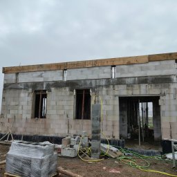 Dawid Wilk TYNK-TECH - Budowa domu z betonu komórkowego w trakcie realizacji. Widoczne ściany, otwory okienne i drzwiowe, drewniane nadproża oraz materiały budowlane na placu budowy.