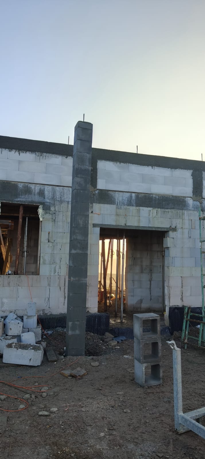 Wznoszenie ściany z betonu komórkowego Ytong. Widoczny fragment ściany, słup z bloczków i rusztowanie. W tle błękitne niebo.