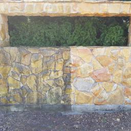 Wyczyść Wymaluj sp. z o.o. - Kamienny mur z oknem, widoczna różnica w czystości połowy muru po zabiegu czyszczenia, zieleń w tle.