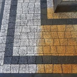 Wyczyść Wymaluj sp. z o.o. - Ułożona kostka brukowa w trzech kolorach: szarym, białym i pomarańczowym, z widocznym fragmentem krawężnika i trawnikiem w tle.