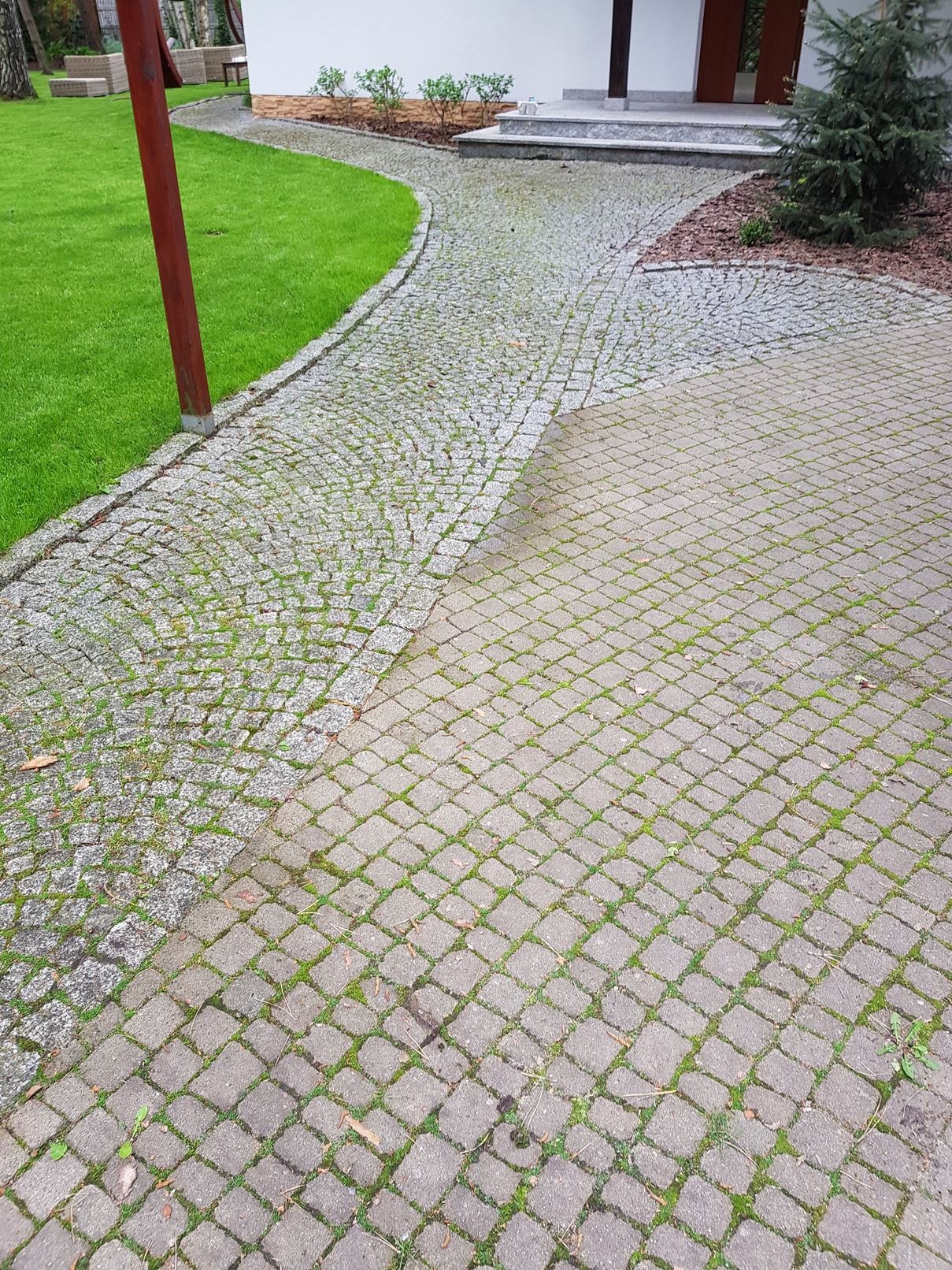 Dwa rodzaje nawierzchni: z kostki granitowej i betonowej, z widocznymi śladami zabrudzeń i mchu, prowadzące do wejścia do budynku.