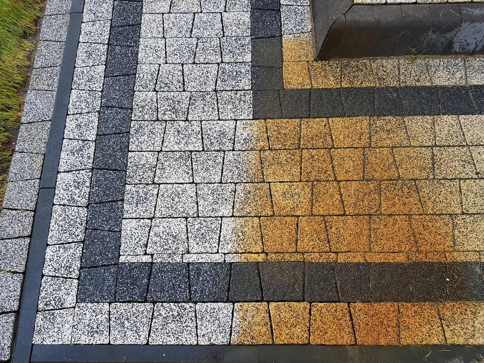 Ułożona kostka brukowa w trzech kolorach: szarym, białym i pomarańczowym, z widocznym fragmentem krawężnika i trawnikiem w tle.