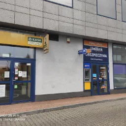 Fasada budynku z punktami usługowymi: Kasa Stefczyka i Unilink Ubezpieczenia z bankomatami przy wejściach.