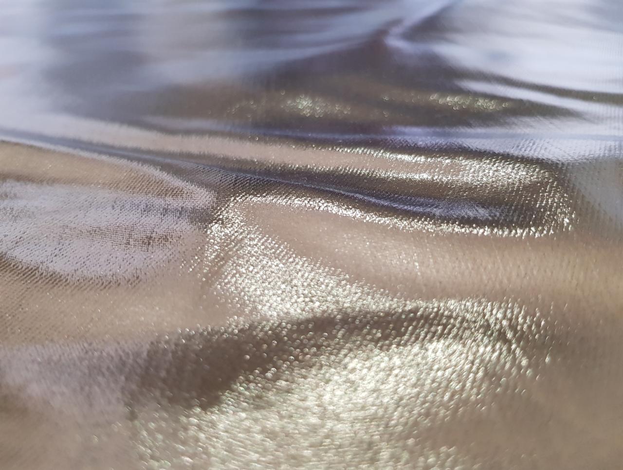 Błyszcząca, złota tkanina z delikatną fakturą, uchwycona pod kątem, ukazująca refleksy świetlne.