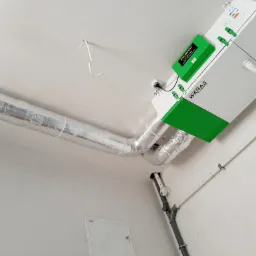 Zamontowana jednostka centralna z rurami izolowanymi folią aluminiową, marki Wanas z zielonym akcentem, widoczna instalacja kanalizacyjna w tle, niedokończone wykończenie sufitu.