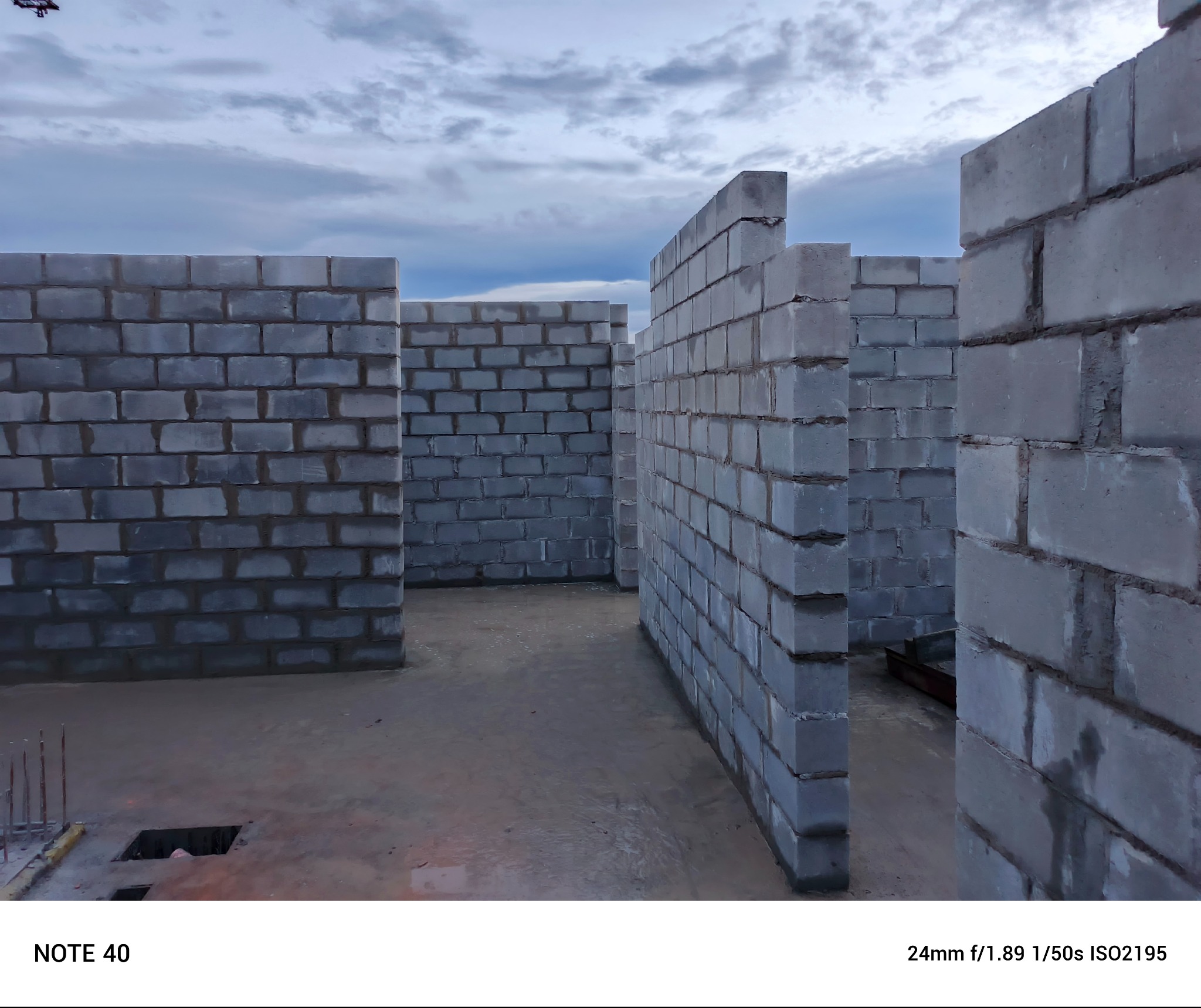 Wznoszone ściany z szarych bloczków betonowych, widok z poziomu podłogi, zarysowane niebo w tle.