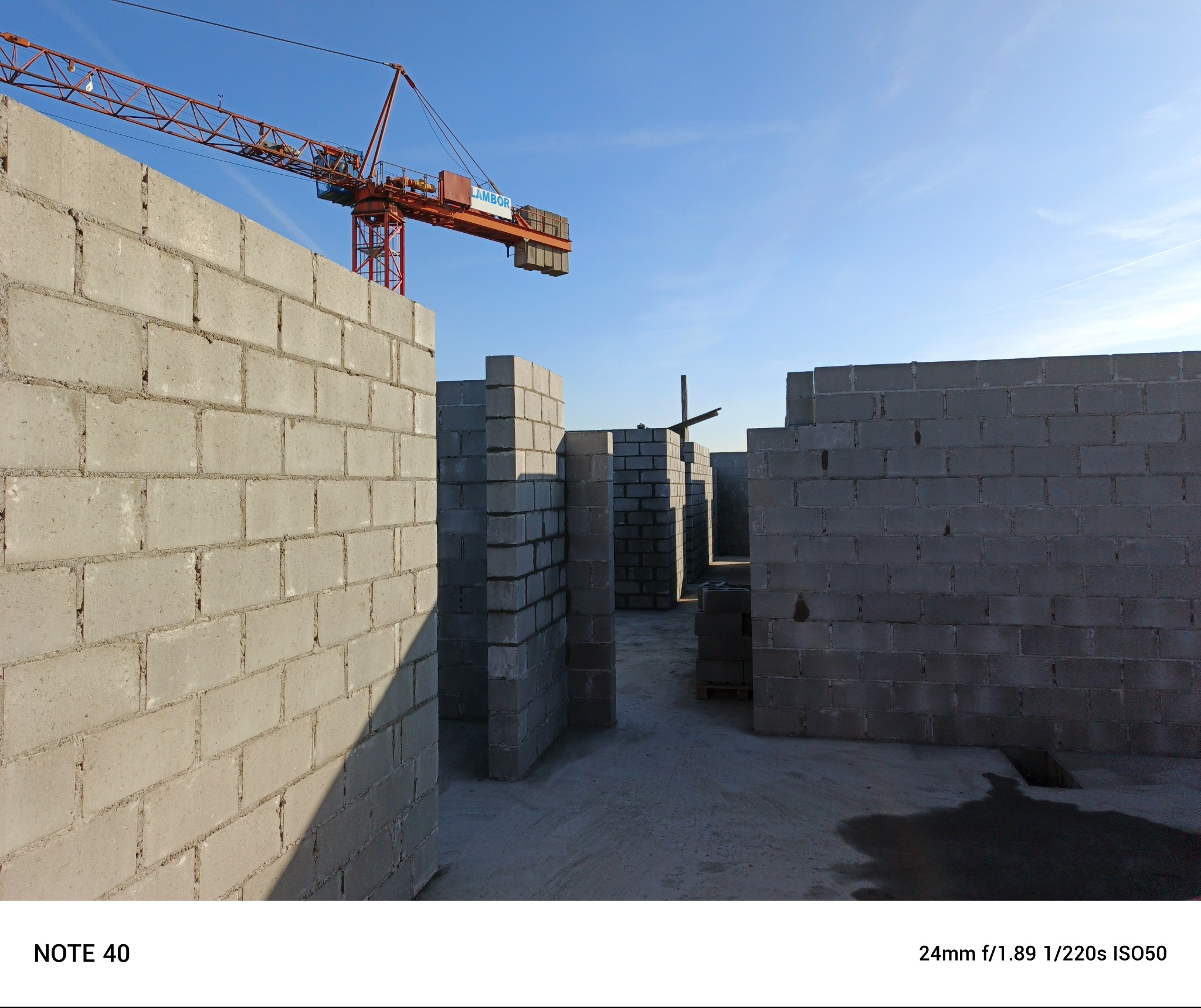 Wznoszone ściany działowe z szarego betonu komórkowego widoczne w perspektywie, z dźwigiem budowlanym na tle jasnego nieba.