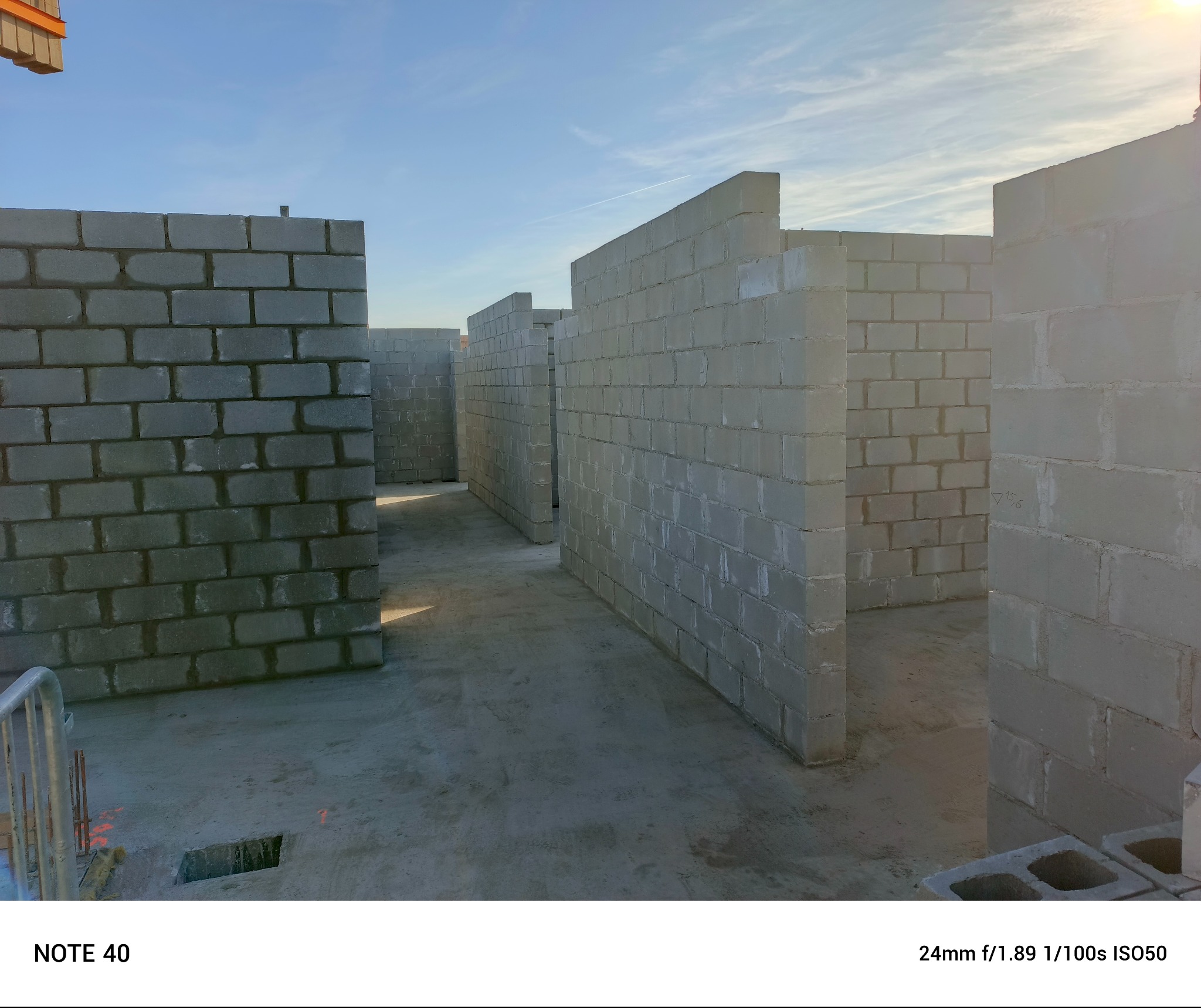 Wnętrze budynku w trakcie budowy z widocznymi ścianami wzniesionymi z szarych bloczków betonowych, surowy betonowy fundament, w tle jasne niebo.