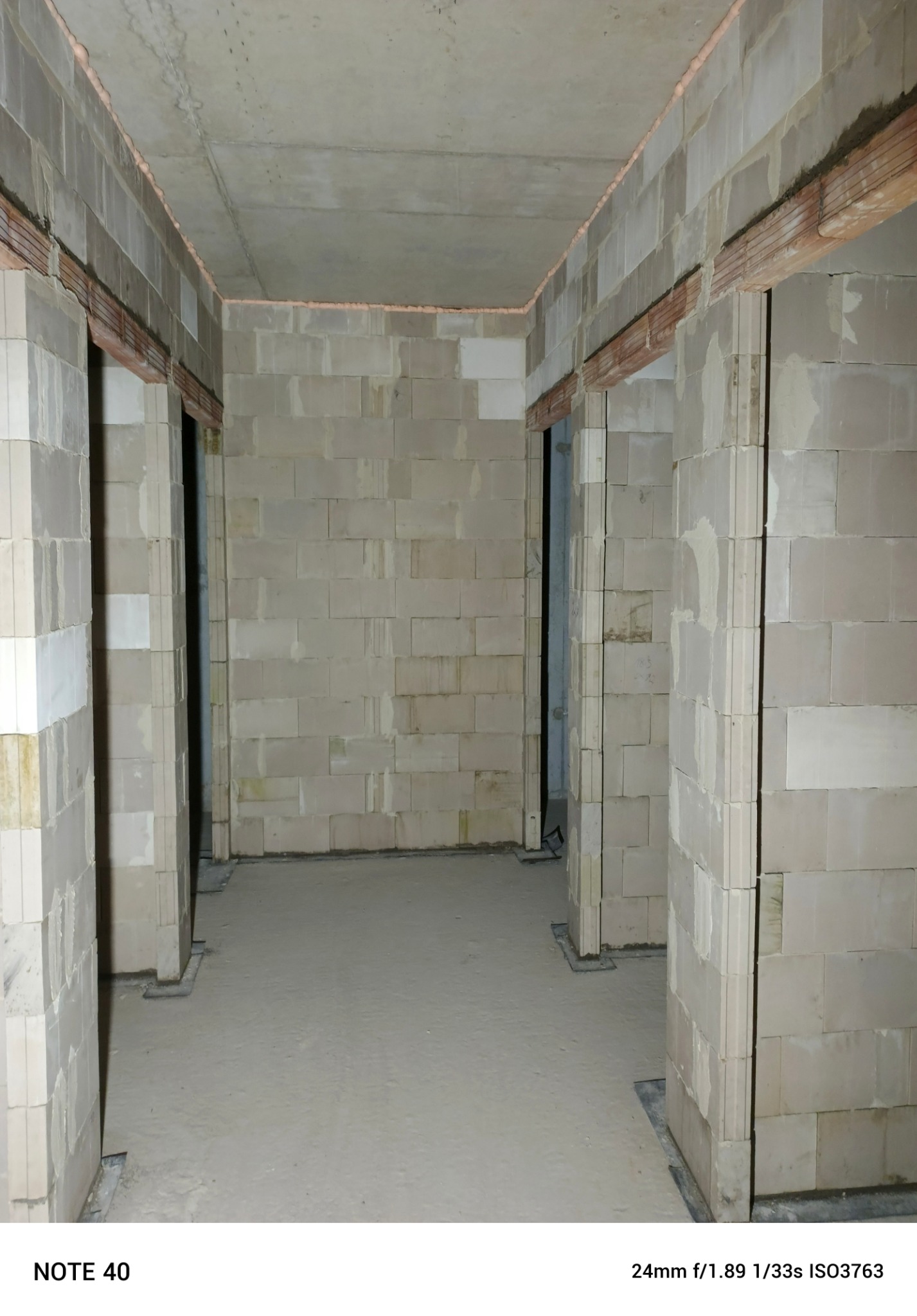 Wnętrze budynku w trakcie murowania ścian z bloczków betonowych, widoczne otwory drzwiowe z nadprożami zbrojonymi, surowy betonowy sufit, ściany w trakcie budowy.