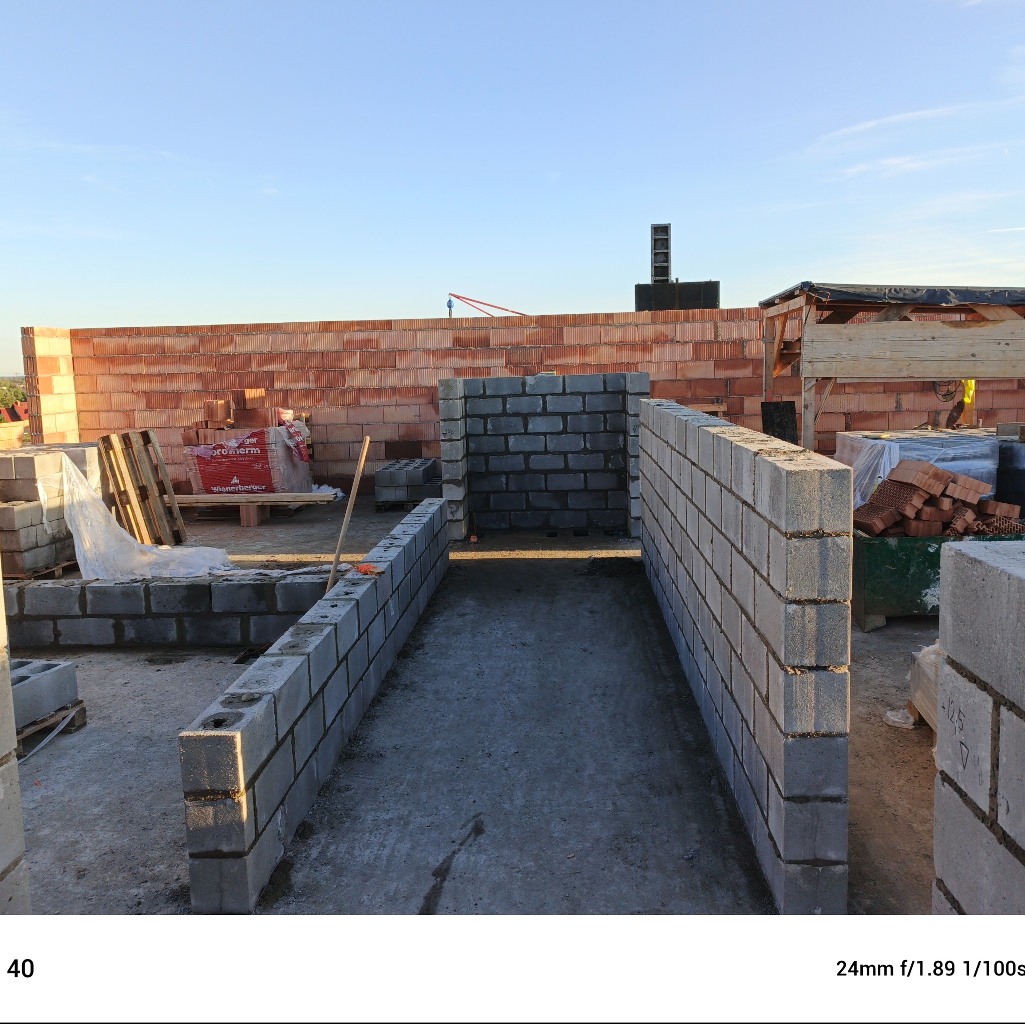 Wznoszenie ścian fundamentowych z bloczków betonowych, widoczne zapasy pustaków ceramicznych Wienerberger Porotherm na palecie, w tle jasne niebo.