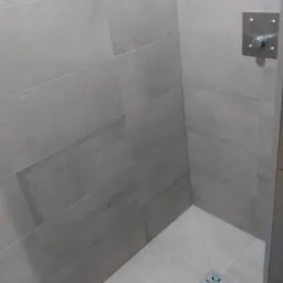 Wykończona kabina prysznicowa z szarymi, poziomymi płytkami na ścianach i jasną posadzką z odpływem liniowym w kształcie gwiazdy.