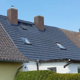 Częściowo odnowiony dach z dach&oacute;wką ceramiczną, z nową powłoką w kolorze antracytowym po lewej stronie i starą, czerwoną po prawej, z trzema kominami i dwoma oknami dachowymi.