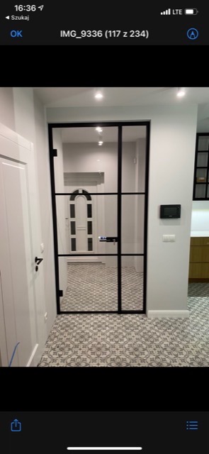 Szklane drzwi z czarnymi szprosami w nowoczesnym wnętrzu, widok na korytarz z wzorzystą podłogą i białe drzwi z łukowym przeszkleniem.