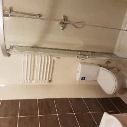 Nowoczesna łazienka z kabiną prysznicową z przesuwnymi drzwiami, białą toaletą z niebieskim logo producenta, grzejnikiem drabinkowym i brązowo-białymi płytkami.