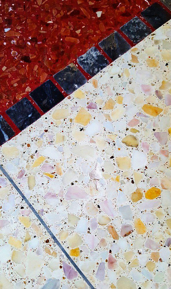 Wielobarwna posadzka lastryko z czerwonym, bordowym i białym marmurem, oddzielona pasem czarnych kwadratowych płytek z czerwonymi fugami oraz cienkim metalowym paskiem.