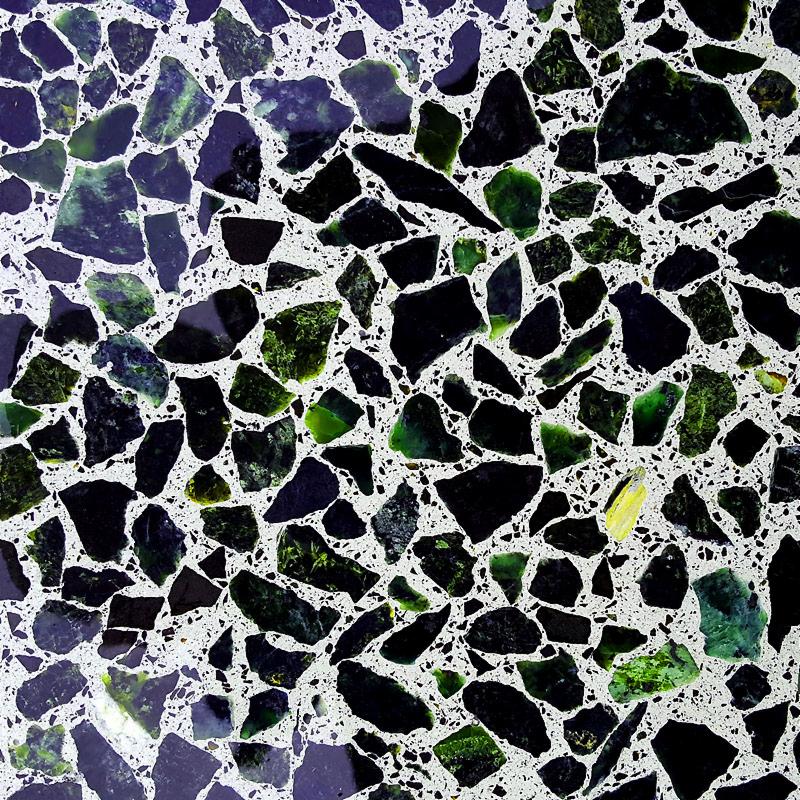 Szlifowana posadzka z fragmentami zielonego i czarnego kamienia zatopionymi w jasnym, drobnym kruszywie, widoczne drobne pęknięcia w spoinach.