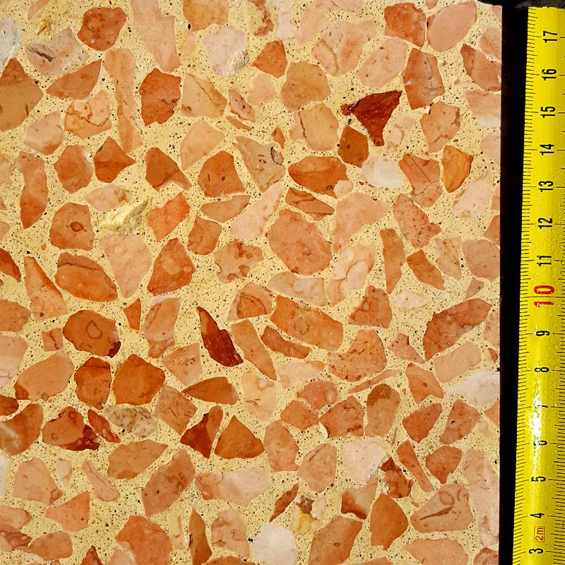 Fragment posadzki z terazzo w odcieniach pomarańczy i beżu, z widoczną miarką w centymetrach, ukazującą strukturę i wymiar.