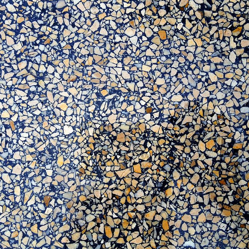 Szczegółowe zbliżenie na posadzkę lastryko z drobnymi, beżowo-brązowymi kamyczkami zatopionymi w ciemnoniebieskim spoiwie.
