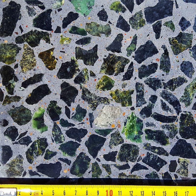 Szlifowana powierzchnia posadzki z zatopionymi fragmentami zielonego i czarnego kamienia, widoczna miarka w dolnej części kadru.