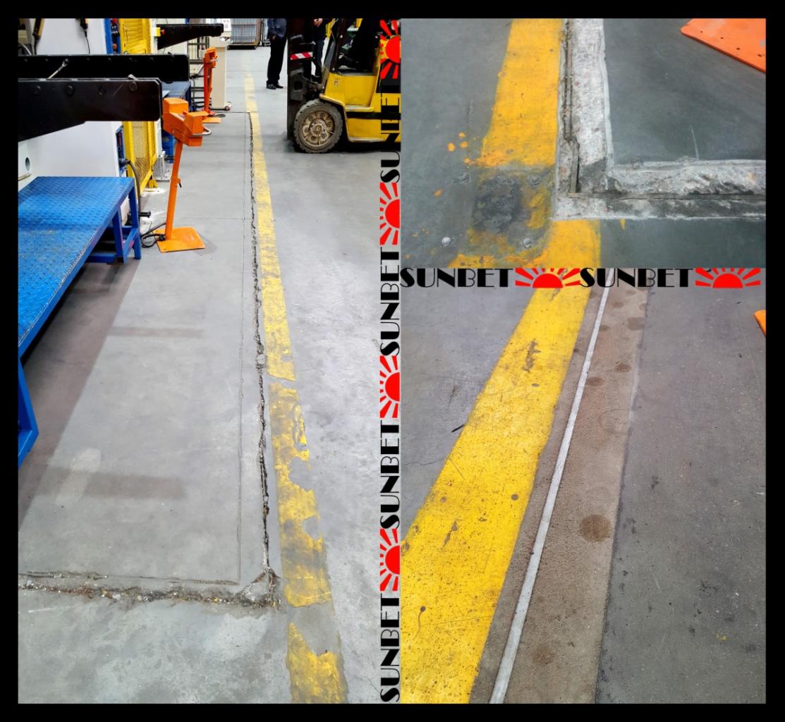 Szara betonowa podłoga w hali produkcyjnej z żółtymi liniami wyznaczającymi strefy, widoczny wózek widłowy i fragmenty maszyn.